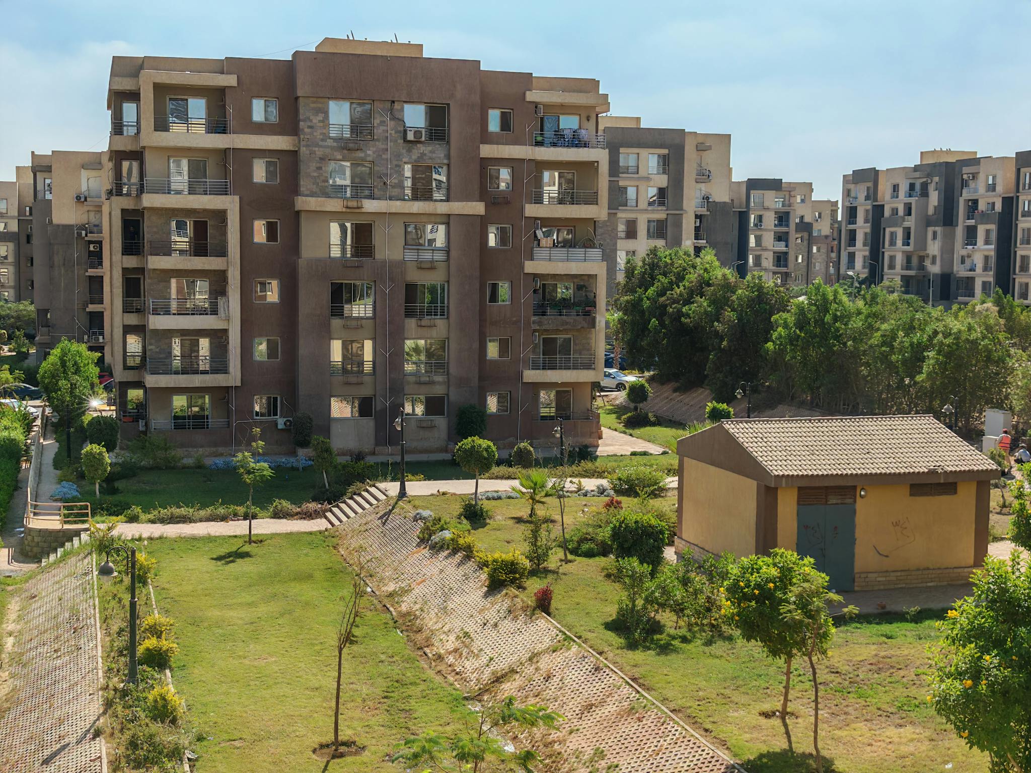 A scenic view of a modern apartment complex surrounded by greenery under a clear blue sky.